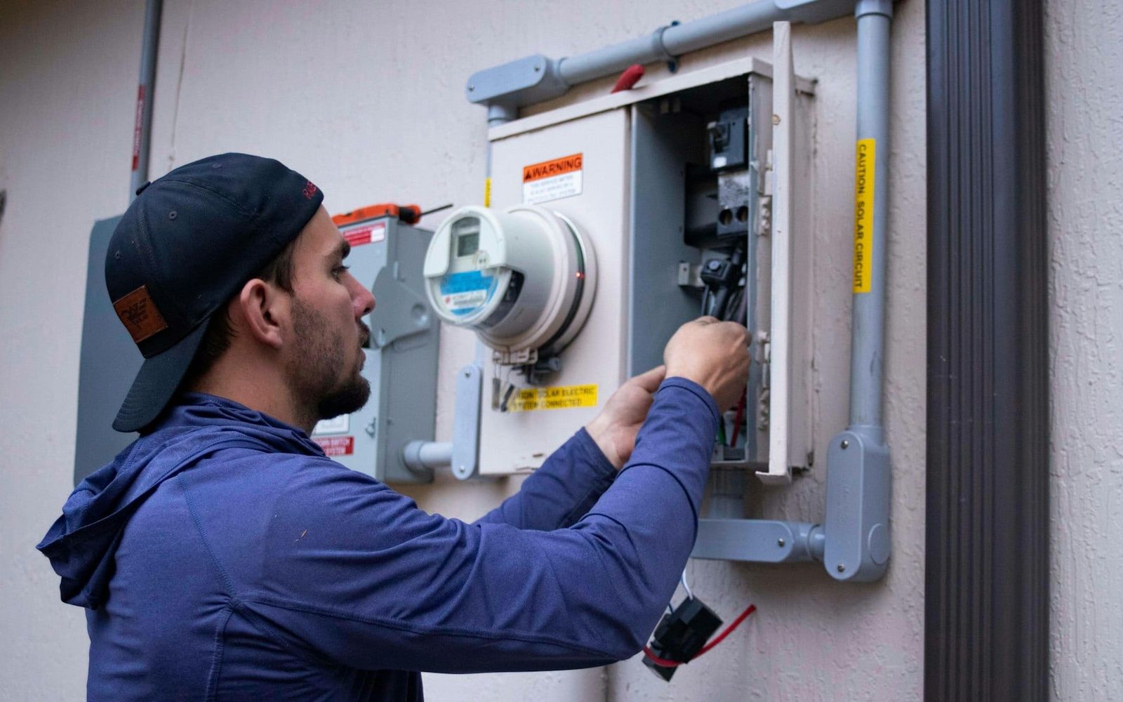 Electrician working inside an outdoor meter and breaker panel