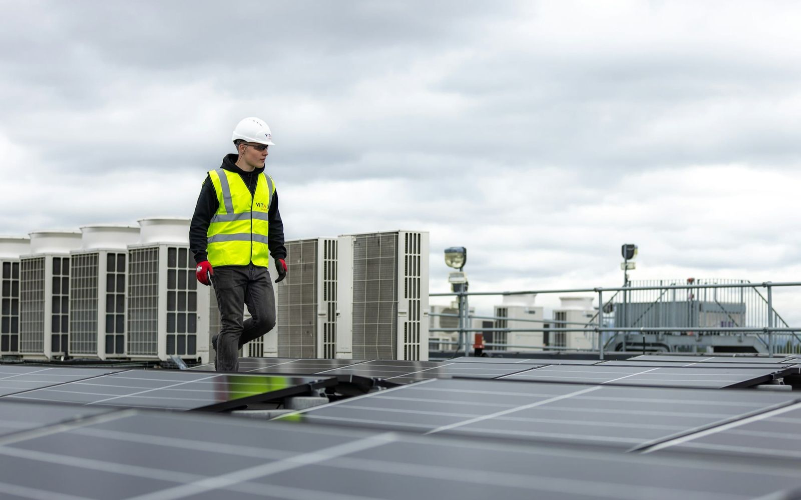 HVAC technician in a hard hat walking past rooftop units