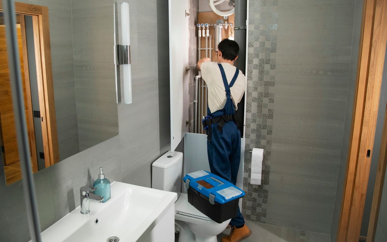 Plumber with a toolbox working on pipes in a bathroom