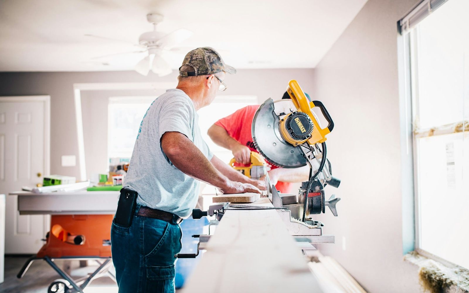 Two renovators cutting trim on a mitre saw inside a house